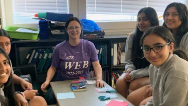 Group of students sitting at a table with teacher completing math game