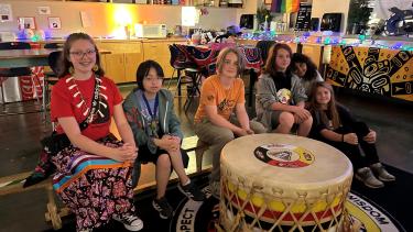 Indigenous Students sitting on a bench in front of a large drum
