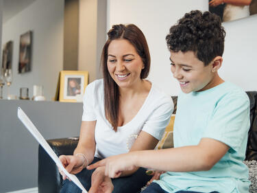 A boy and his mother are looking at the child's report card together at home.