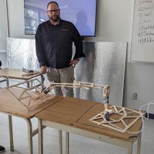 Two female students working their constructed design in Engineering class, male teacher stands and watches